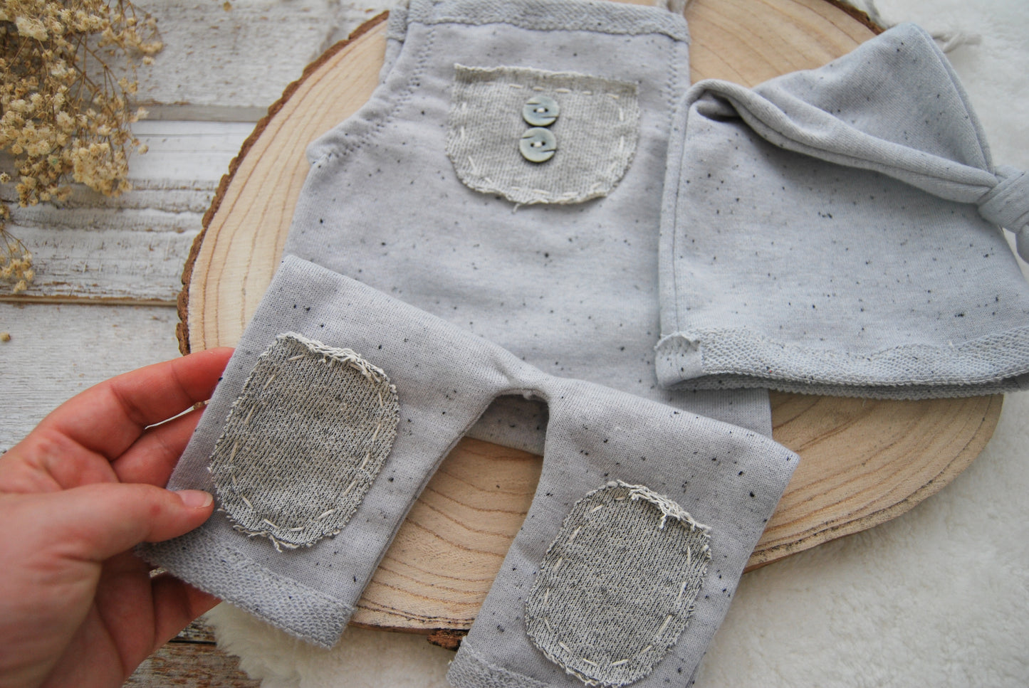 Gray textured romper with button details and knee patches held over a wooden surface