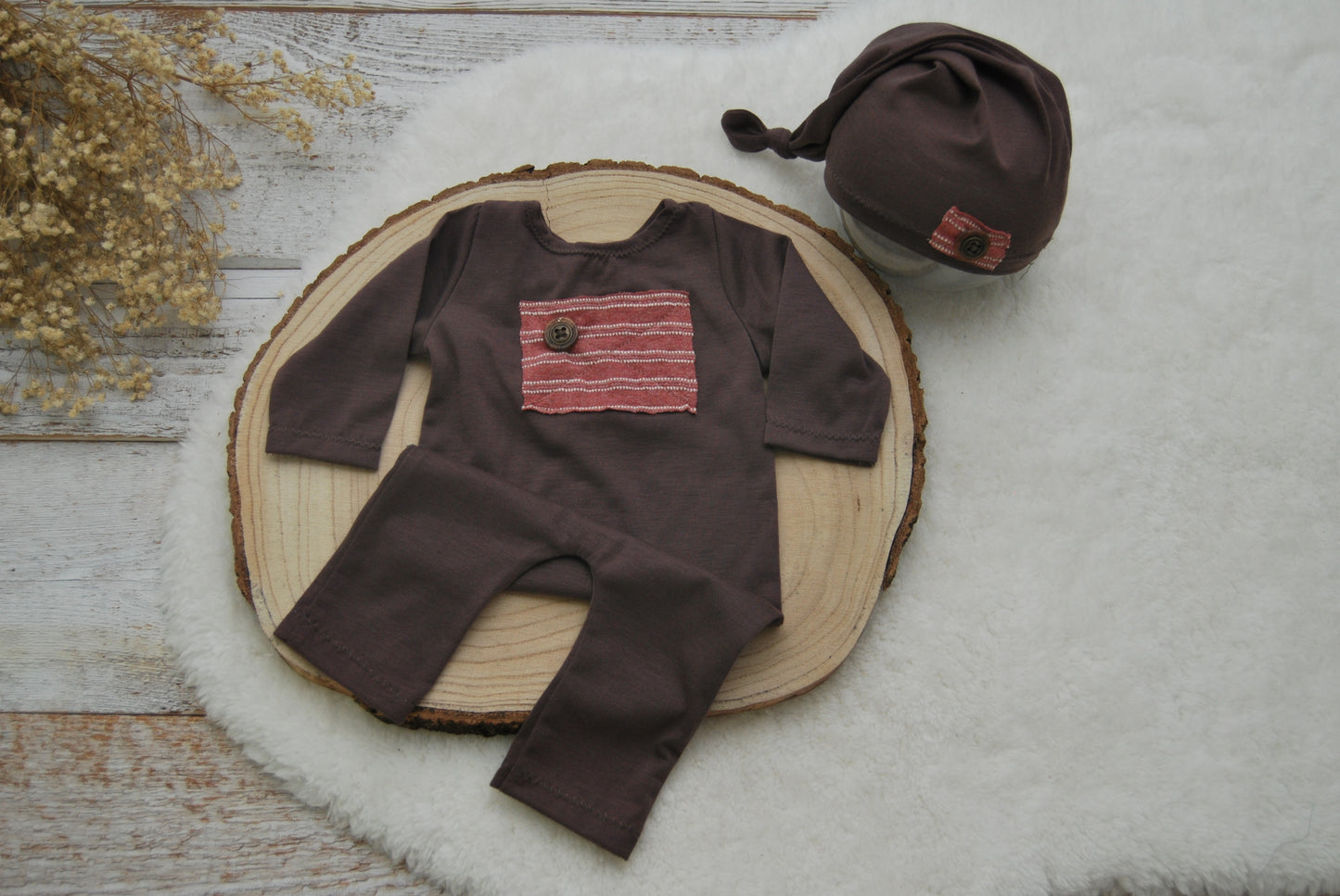 Brown baby outfit with red pocket and matching hat on a wooden surface