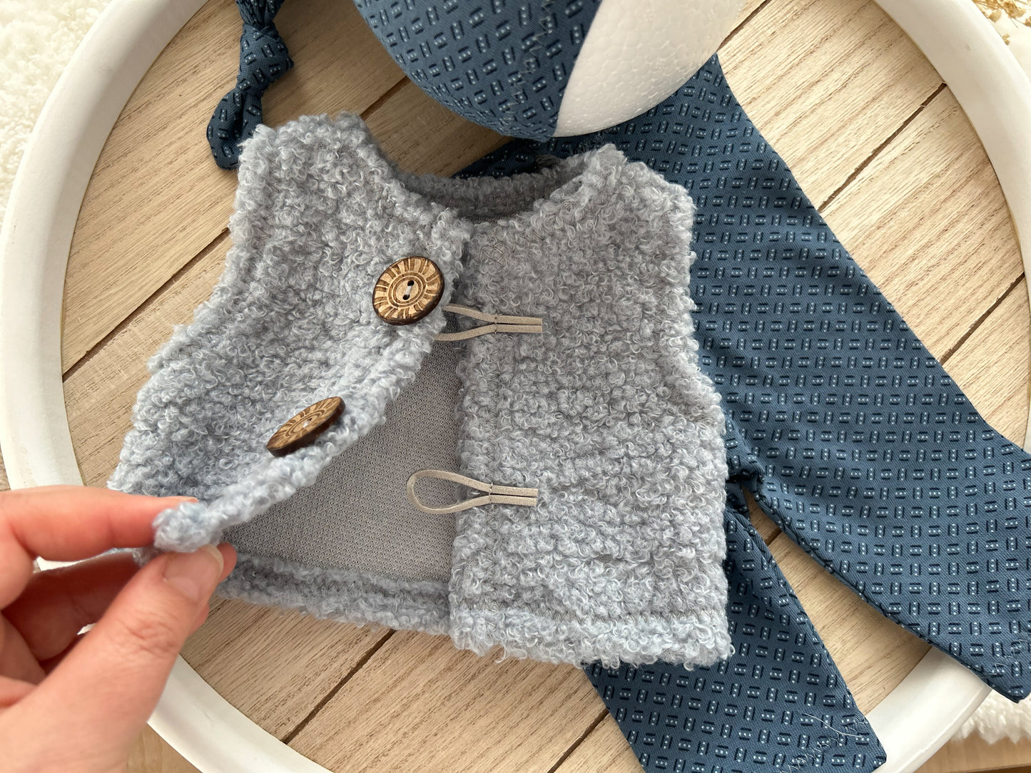 Small gray knitted vest with buttons held by a hand on a wooden surface.