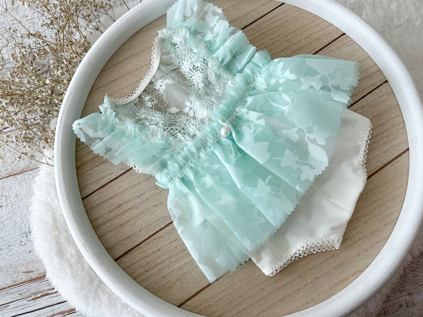 The back of the floral newborn romper in ivory and light mint green with ruffles