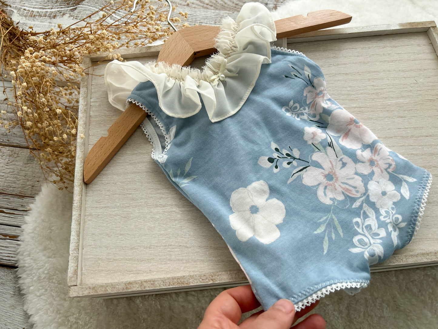 Newborn girl romper in blue fabric with floral print. It features ivory chiffon ruffles around the neckline. Ideal as newborn photo prop.