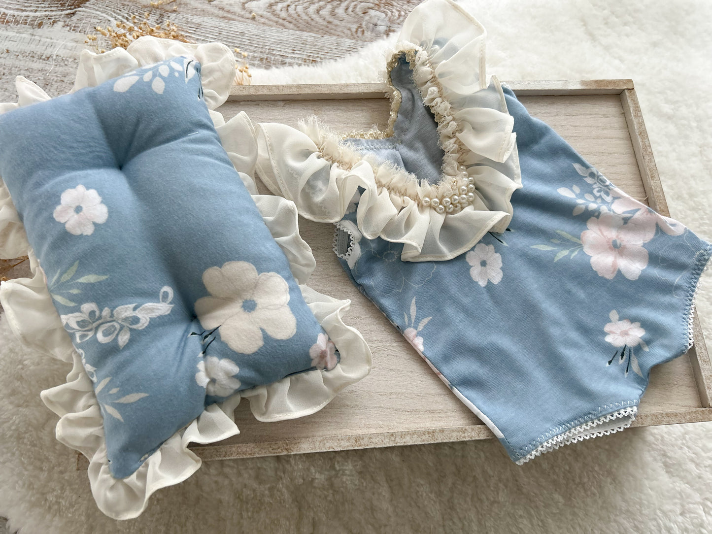 Newborn romper and posing pillow displayed on a wooden tray
