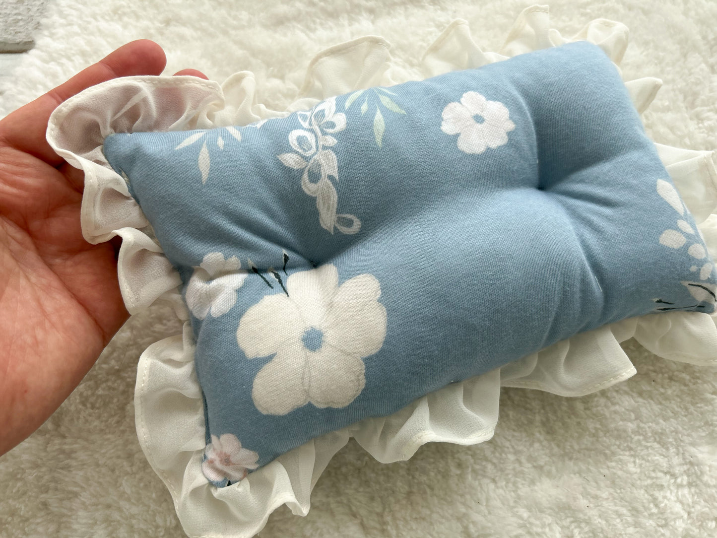 Newborn posing pillow in blue color with white floral pattern and ruffles.