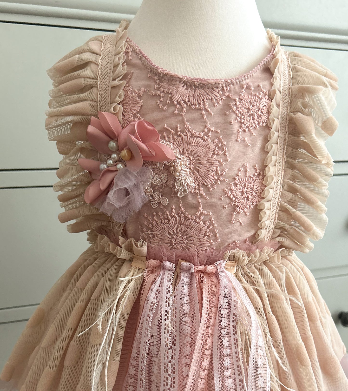 Pink lace dress with floral details on a mannequin against a white background