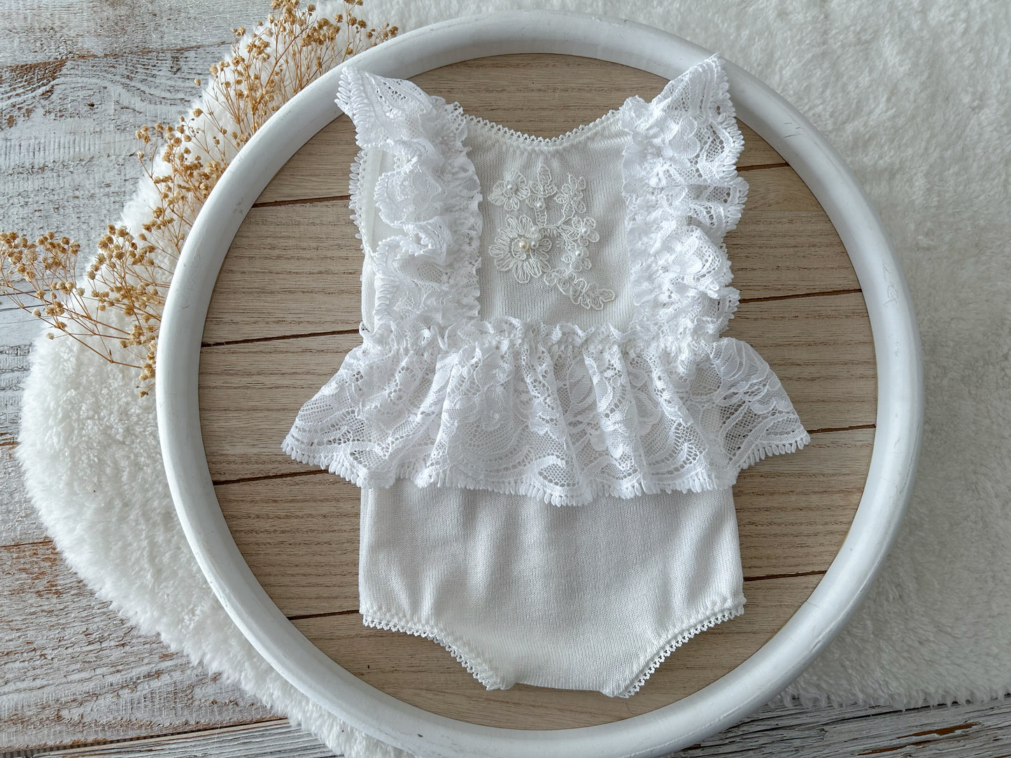 White newborn romper with ruffled lace sleeves and skirt displayed on a round tray