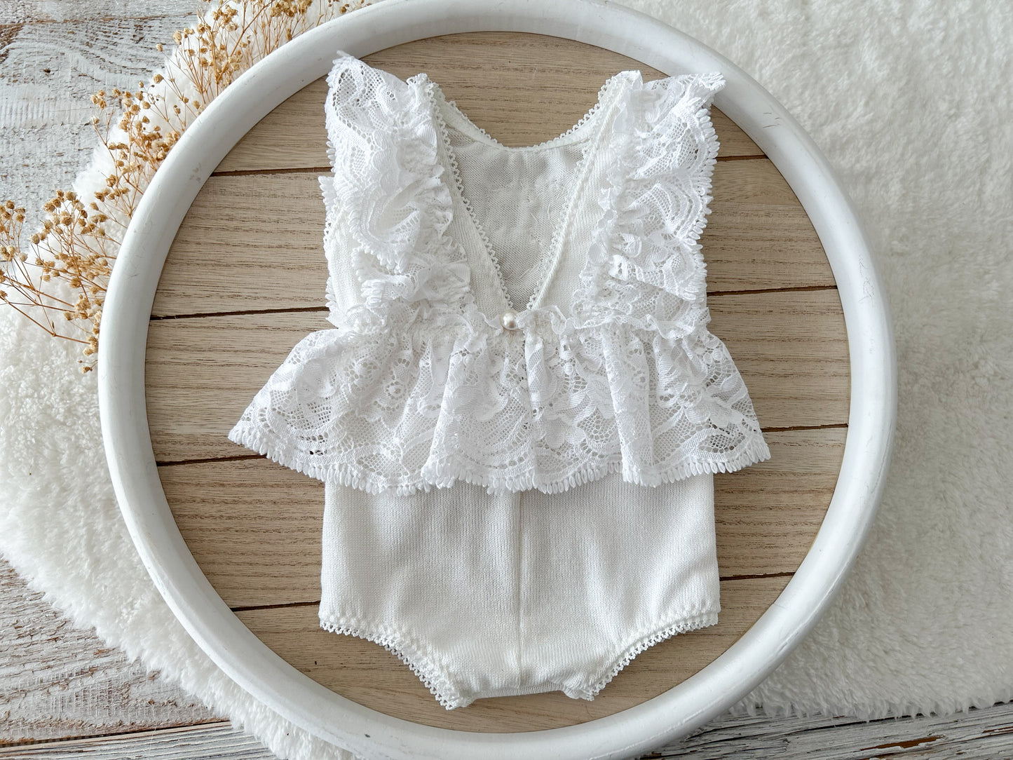 Back view of the white romper with V cut and pearl button closure on wooden surface