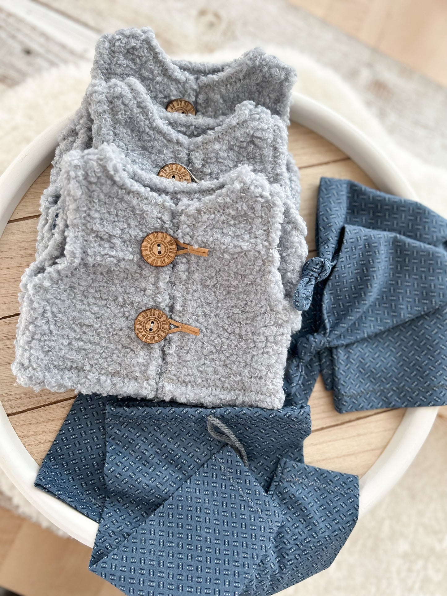 Gray knitted vest with wooden buttons and blue pants on a white circular surface.