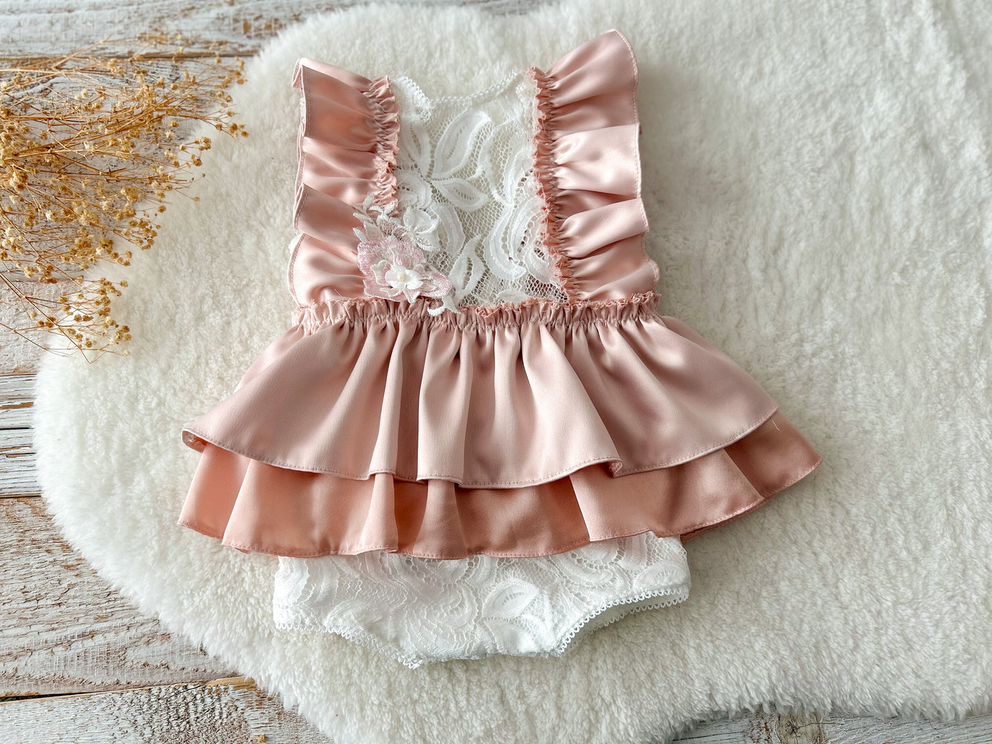 Peach satin and lace baby romper with ruffle details, displayed on soft background
