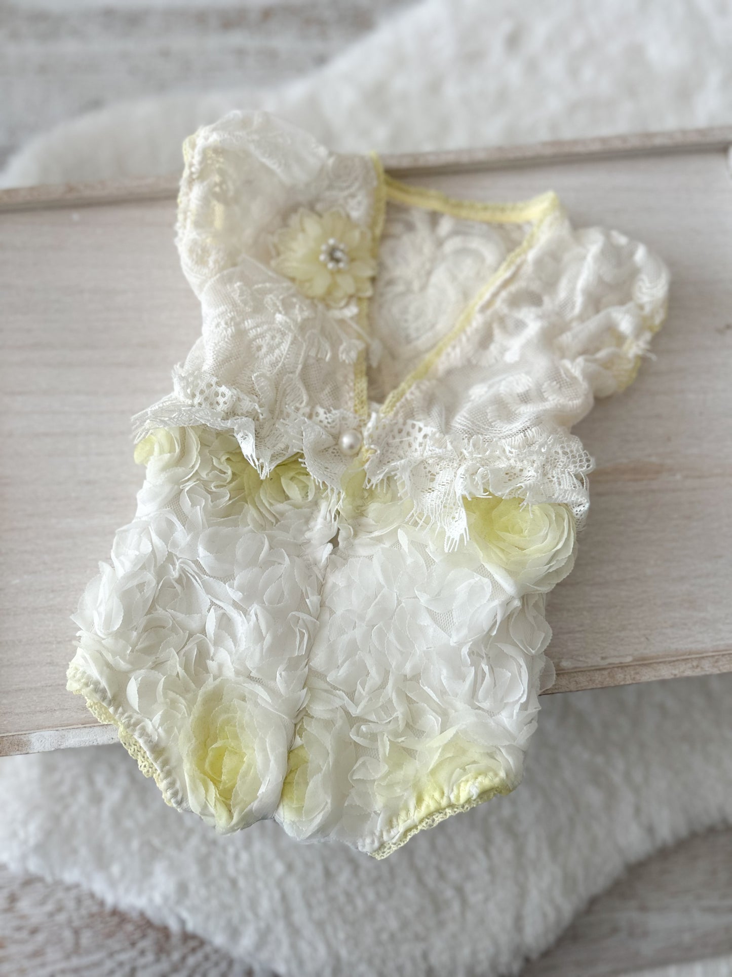 Delicate lace baby romper with floral details on a wooden surface