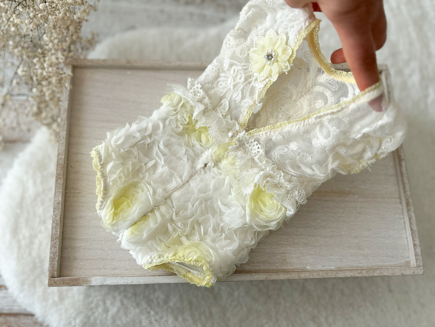 White lace garment with yellow accents held over a wooden frame.