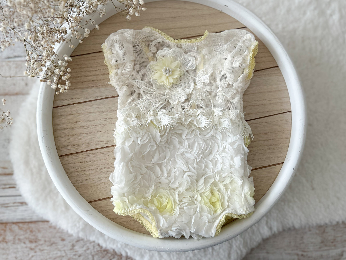 Delicate floral baby romper on a wooden surface with decorative elements.