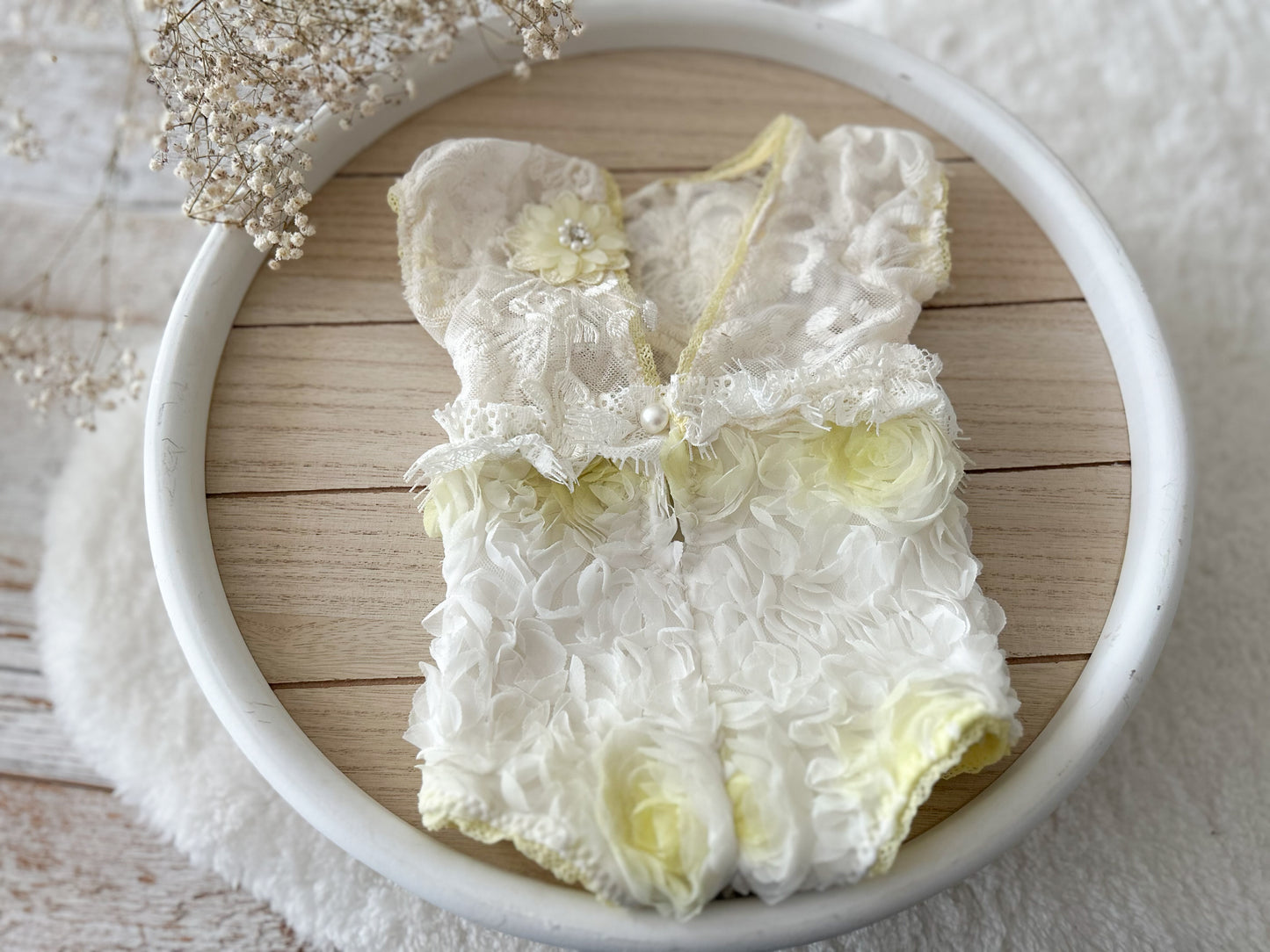 White lace baby romper for photography with yellow accents on a wooden surface