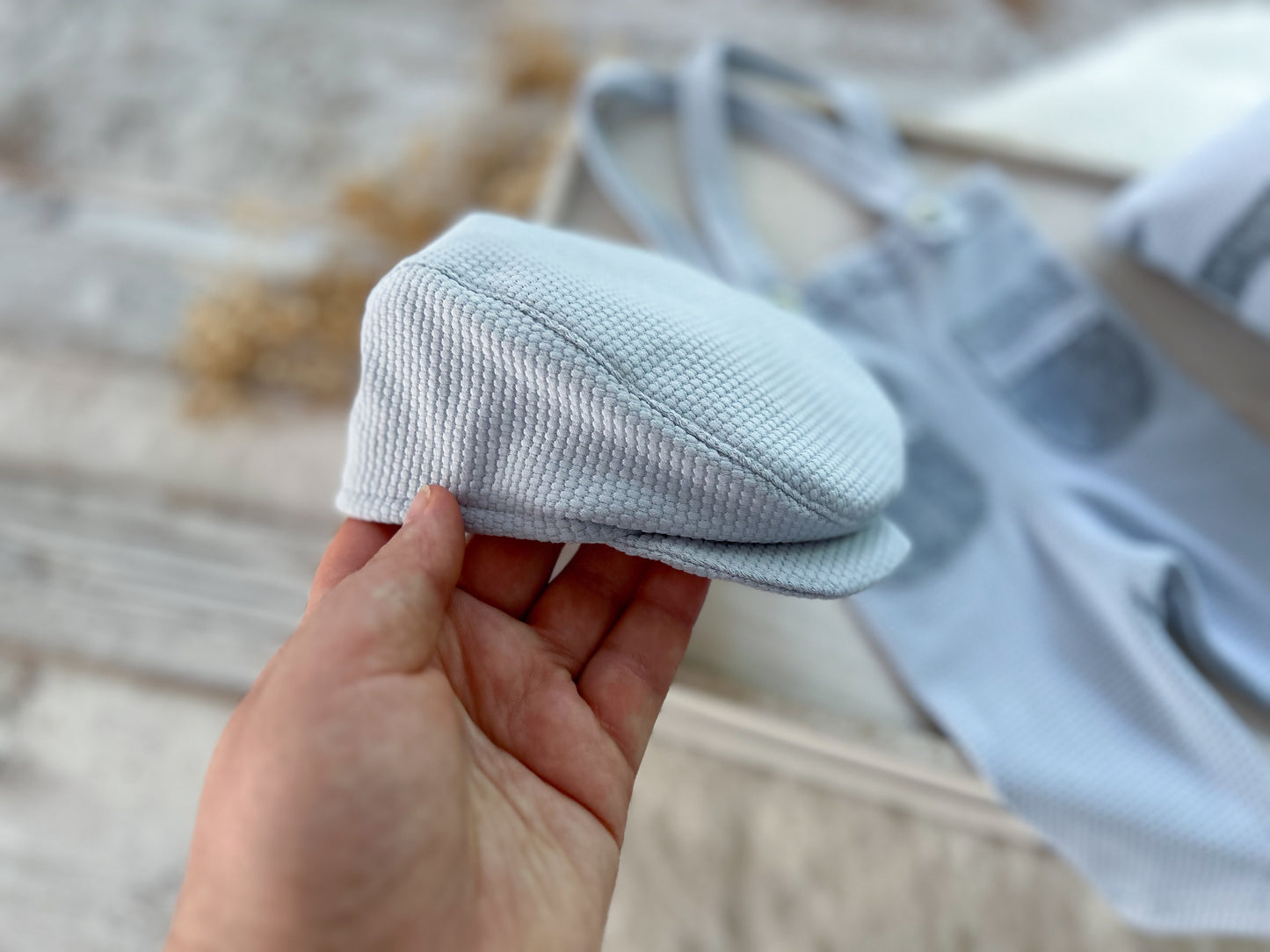 Hand holding a textured light blue newsboy cap for photography shoots.