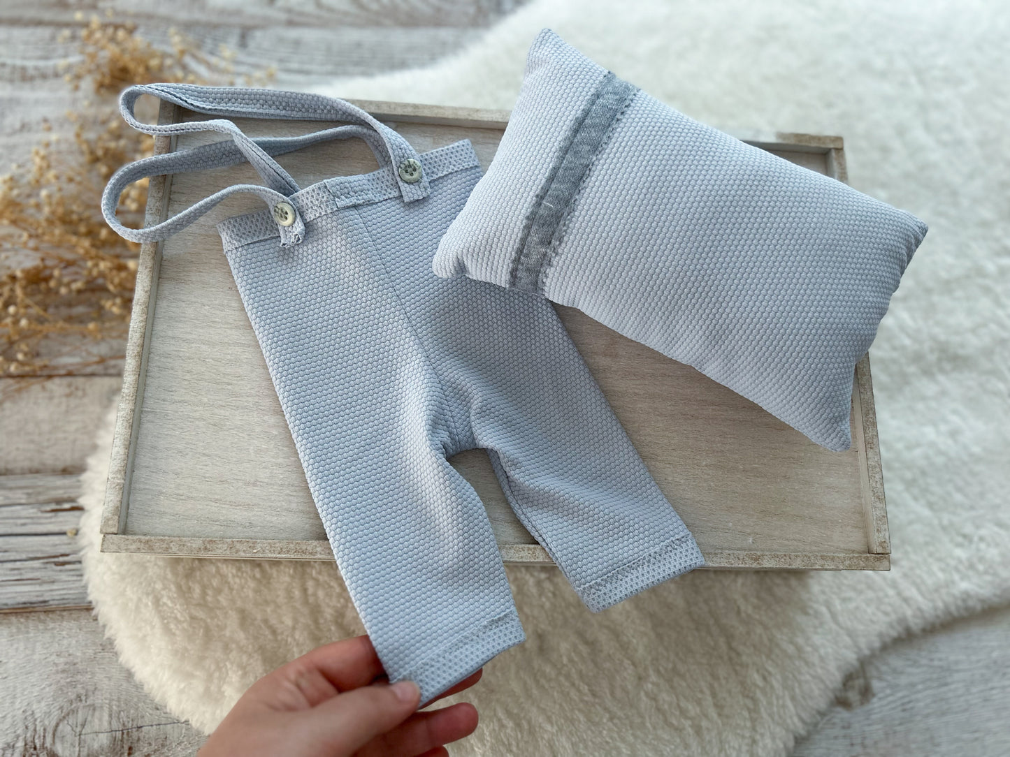 Baby outfit with shorts and bib on a wooden tray, held by a hand.