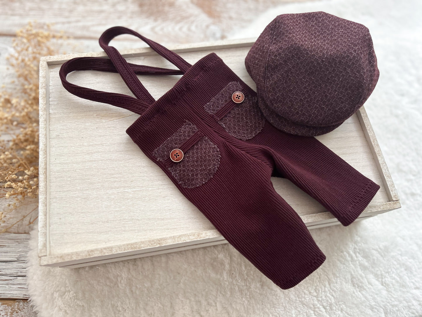 Maroon baby outfit with suspenders and hat on a wooden surface