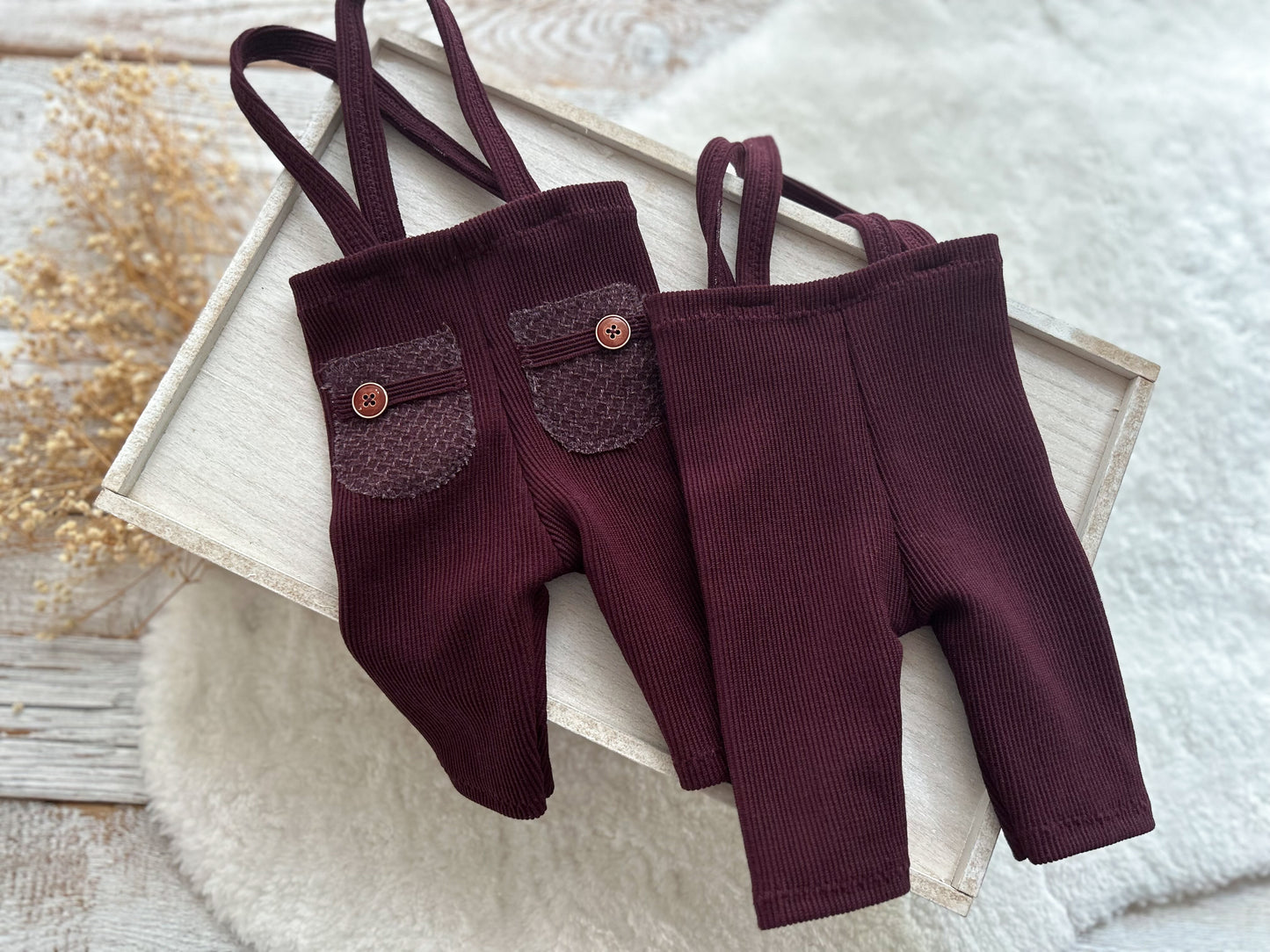 Pair of maroon suspenders with buttons on a textured surface for newborn boy photography shoots