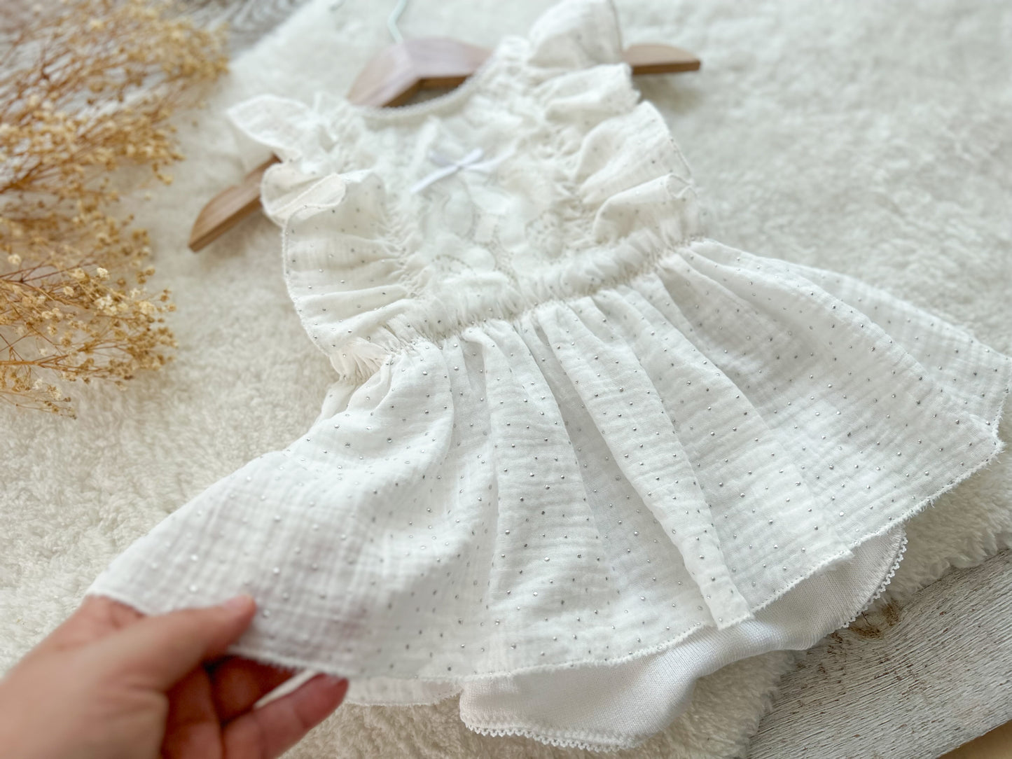 White baby romper with ruffled details held by a hand on a textured surface.