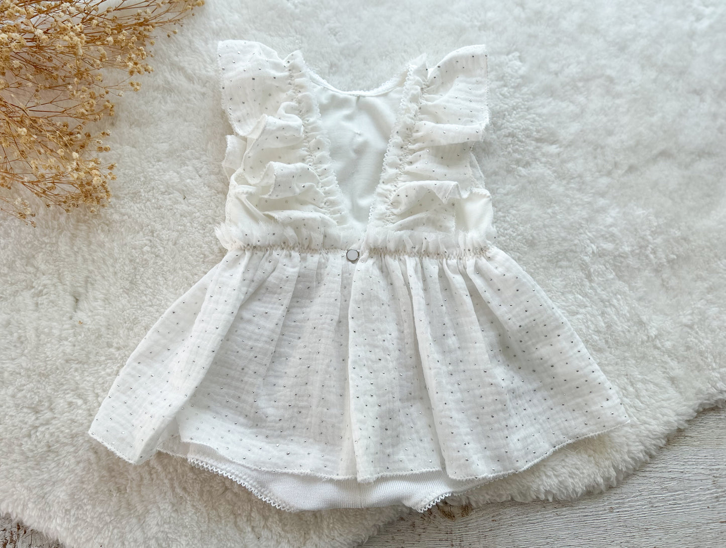 The back of a white muslin sitter photography dress that closes with pearl button