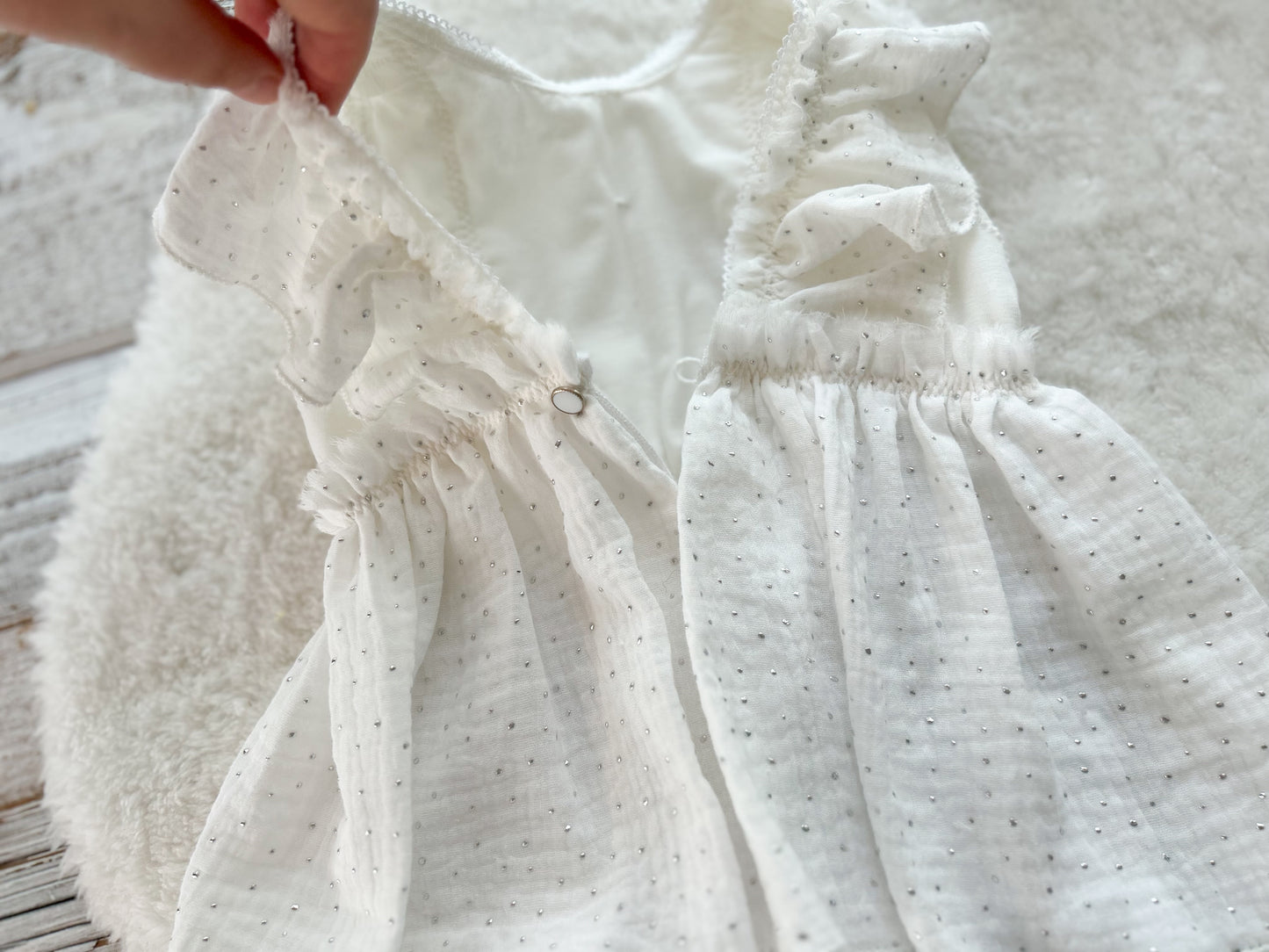 Close-up of a white baby dress with ruffled details on a wooden surface