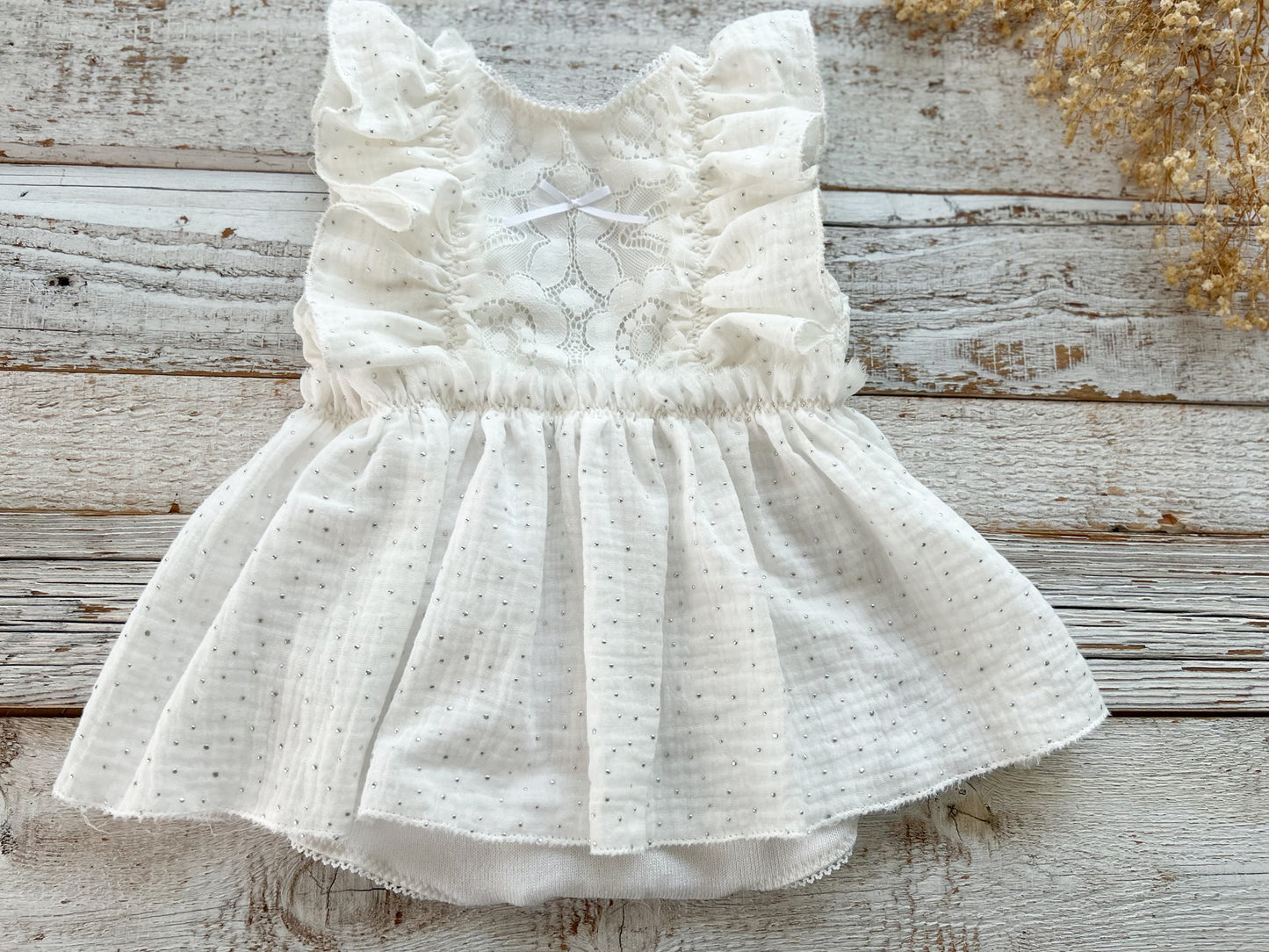 Flat lay view of white sitter romper with dotted muslin skirt and ruffled details