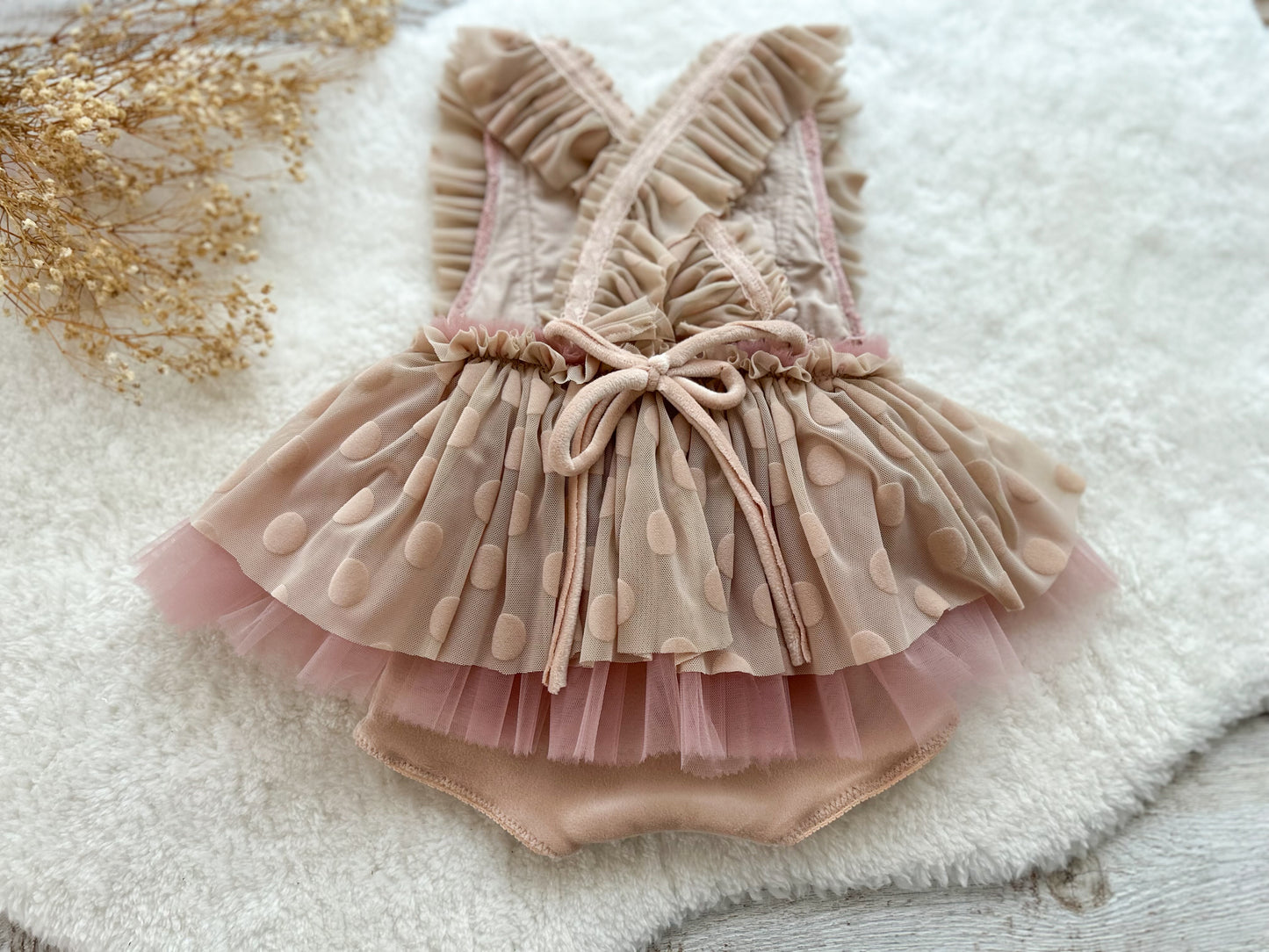 Back view of baby girl romper featuring crisscross ruffled straps and soft polka dot mesh skirt in blush tones.