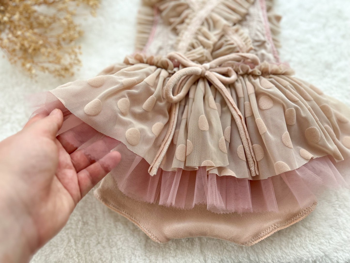 Pink polka dot dress with a hand holding it against a textured white background