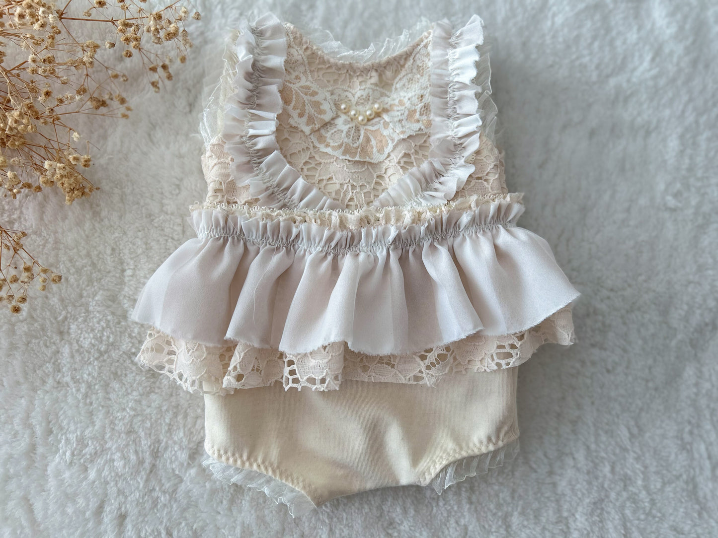 Flat lay of cream lace newborn outfit on wood backdrop