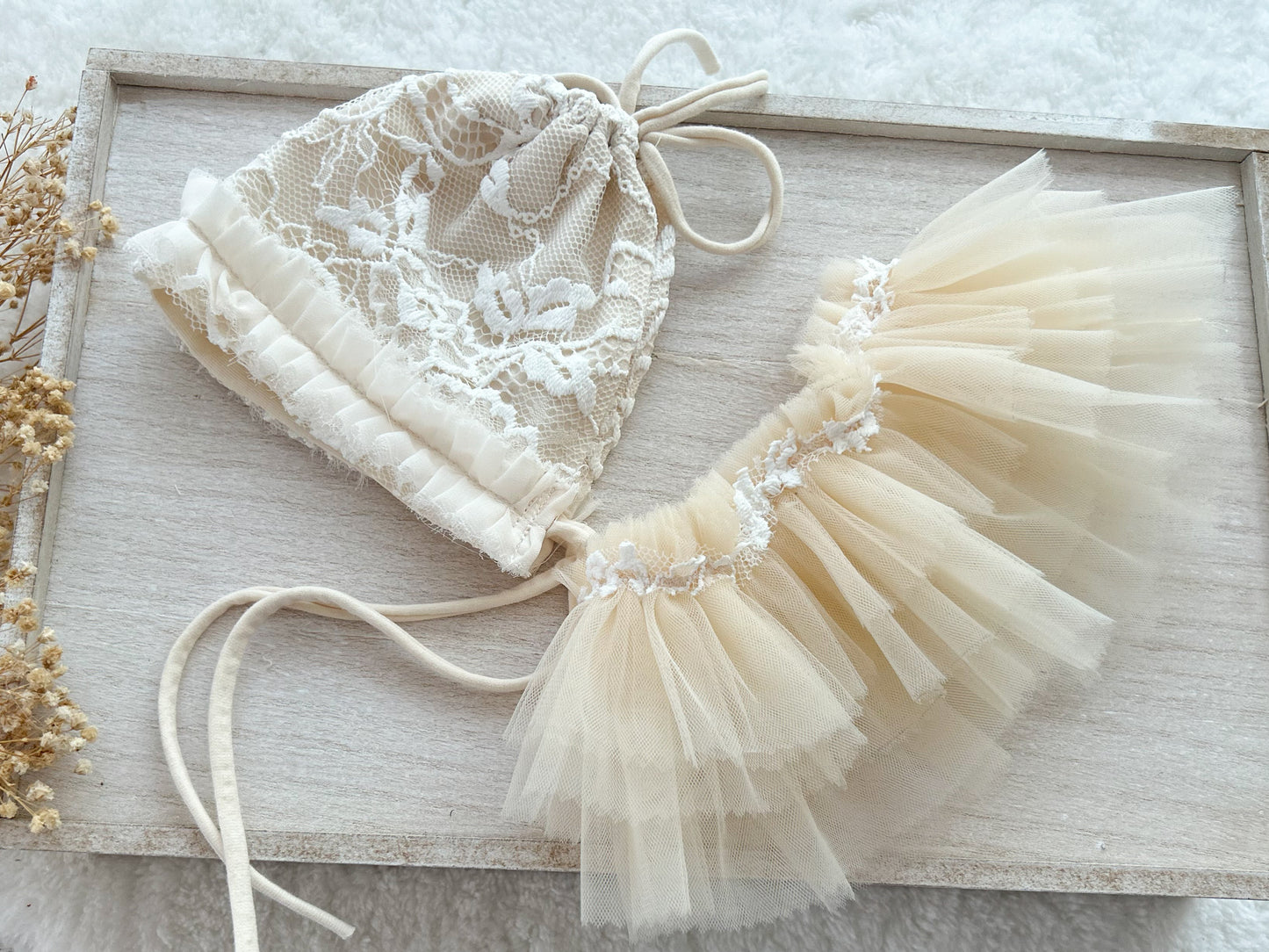 Newborn lace bonnet and tutu skirt on a wooden tray.
