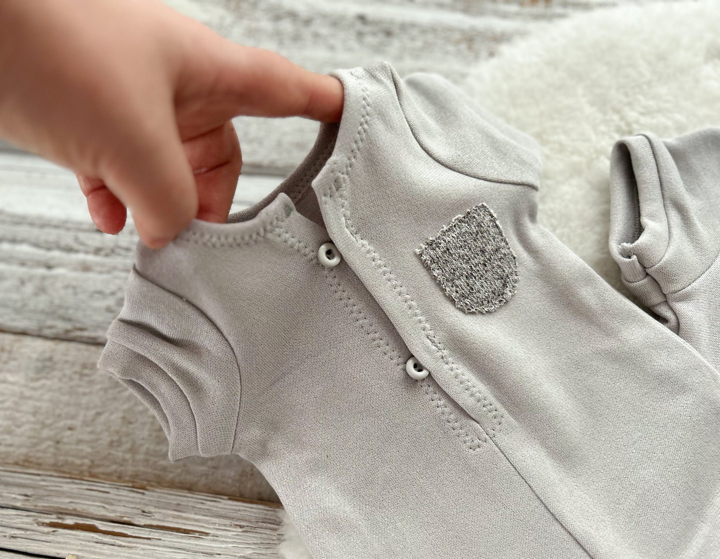 Close-up of a baby onesie with a hand adjusting the straps on a wooden surface
