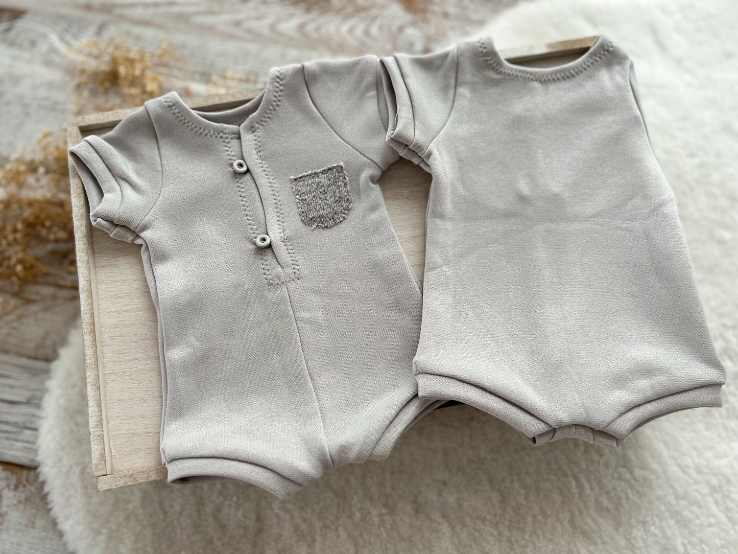 Gray baby romper with short sleeves and pants on a textured surface