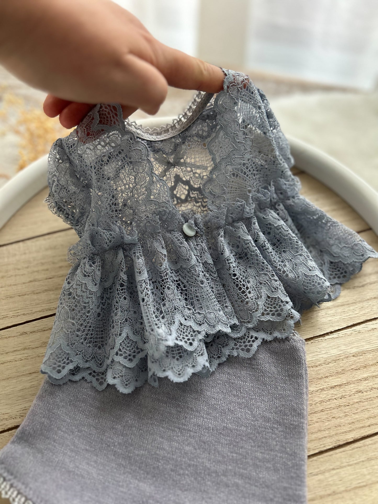 Gray lace-trimmed baby dress on a wooden surface with a blurred background