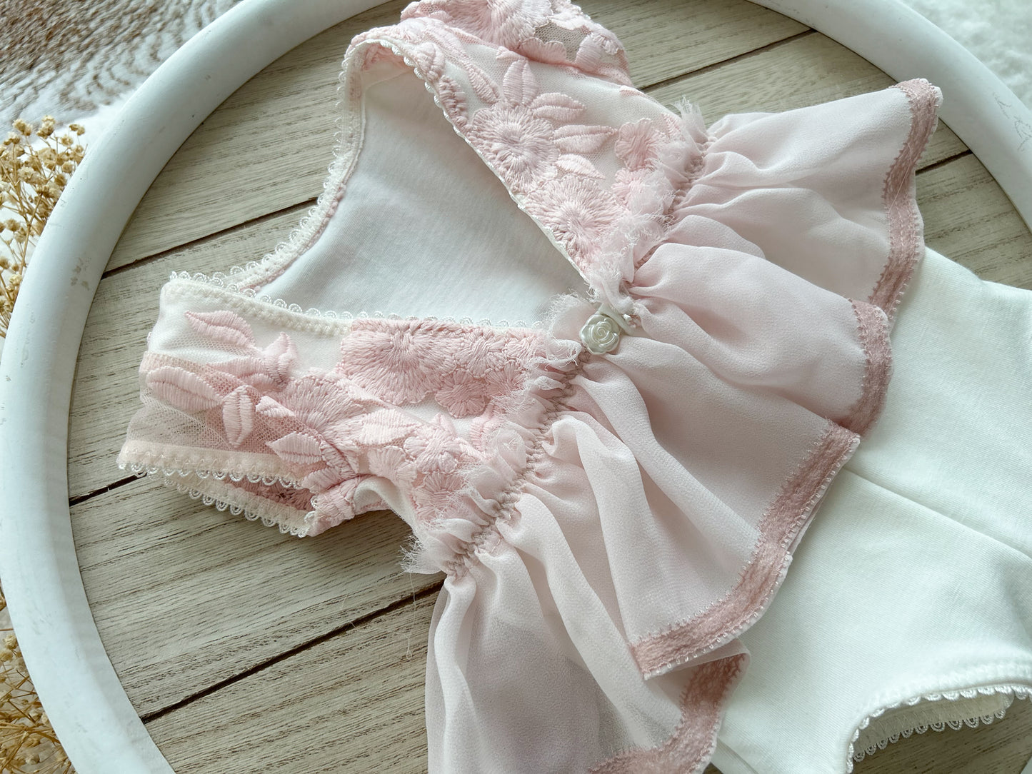 Close up on the back of the pale pink newborn girl romper, cut in V shape and with a rose pearled button