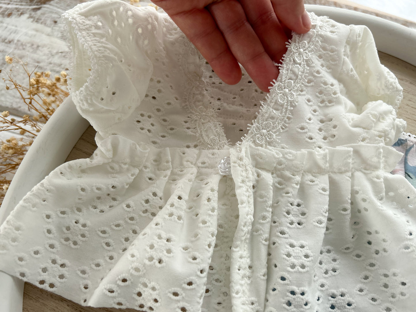 White embroidered baby girl photo outfit held by a hand on a light background