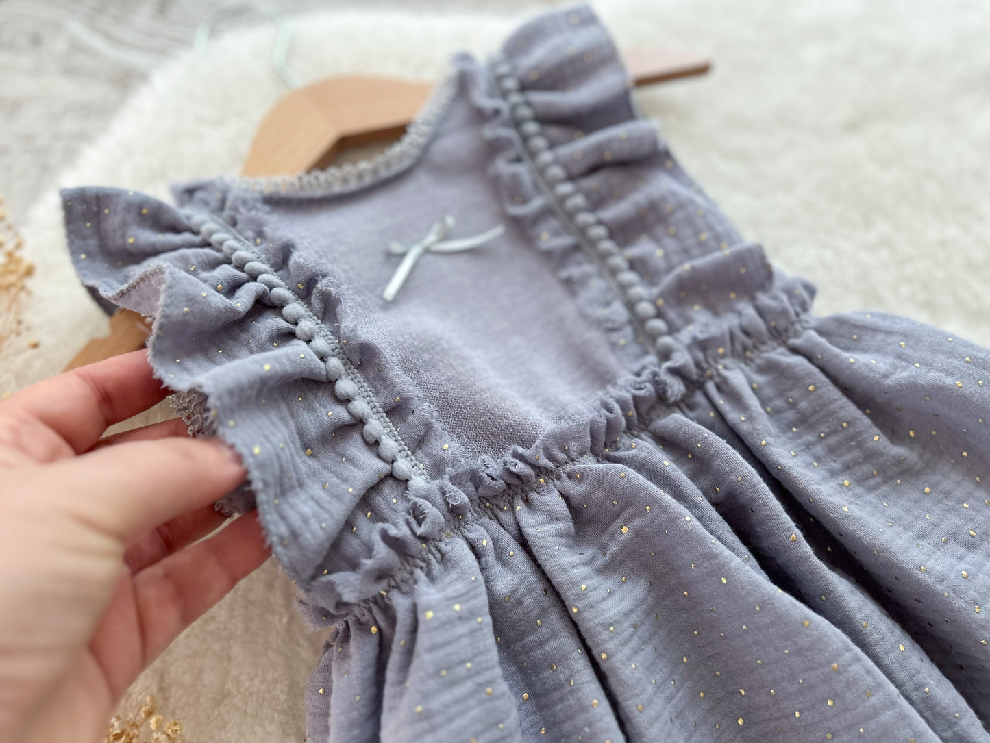 Sitter photo dress, gray dress with ruffled details held by a hand on a neutral background