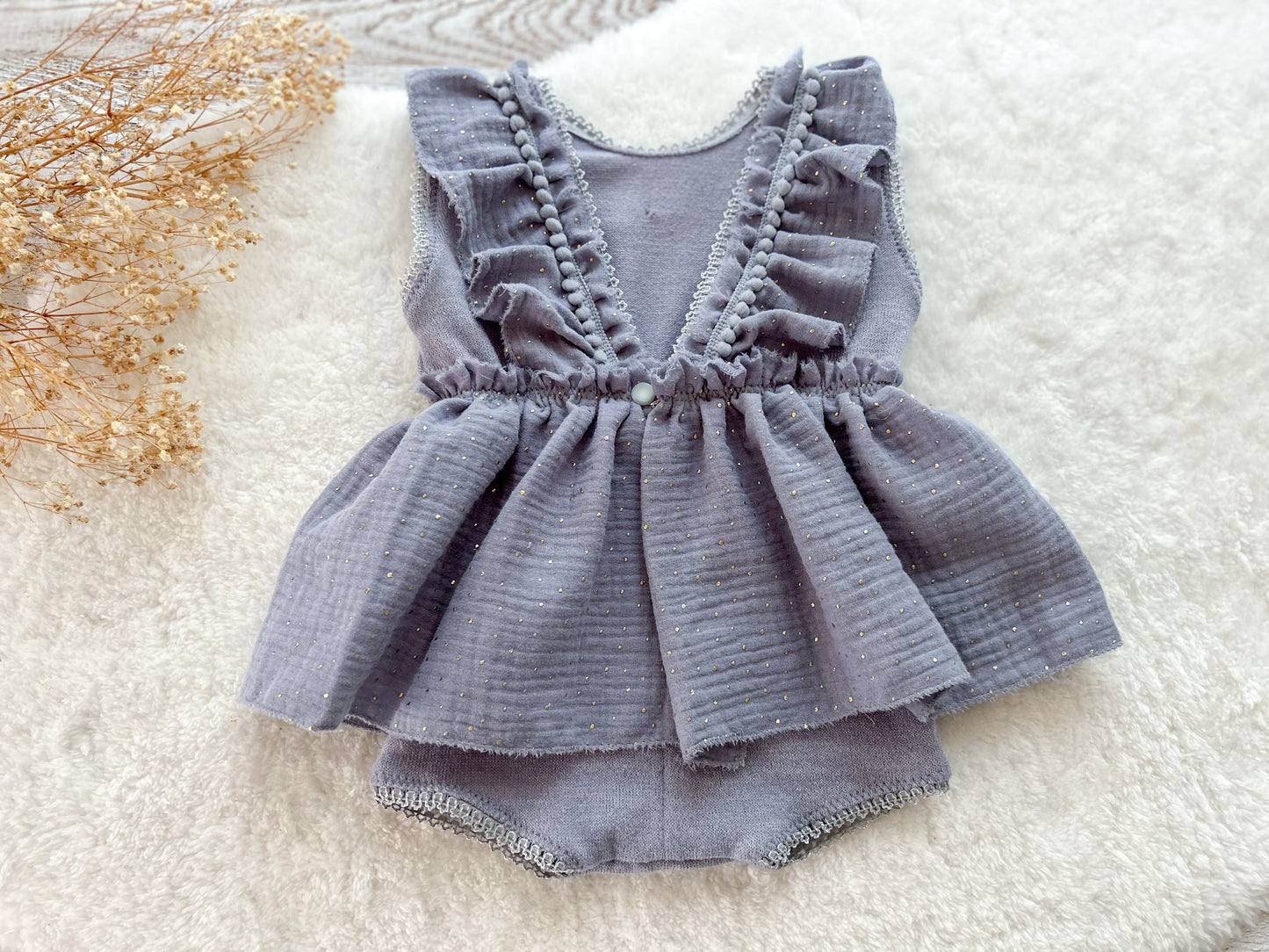 Gray baby romper with ruffled details on a white surface