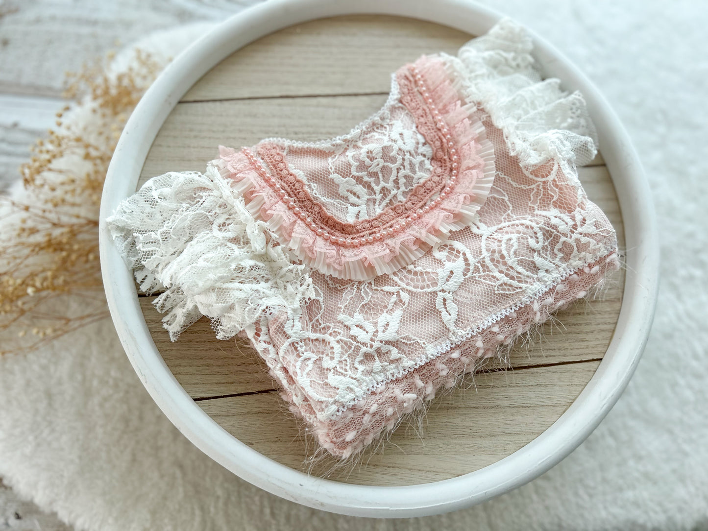 Pink lace baby outfit on a wooden surface with a white bowl
