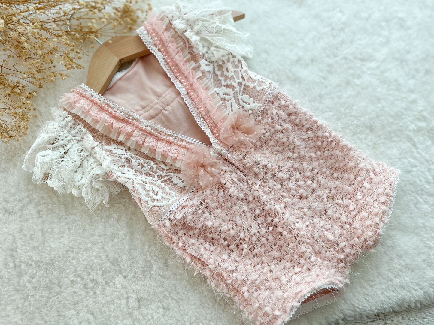 Back of pink baby romper with V-cut, pearl trim, and tied organza bows on a white textured surface.