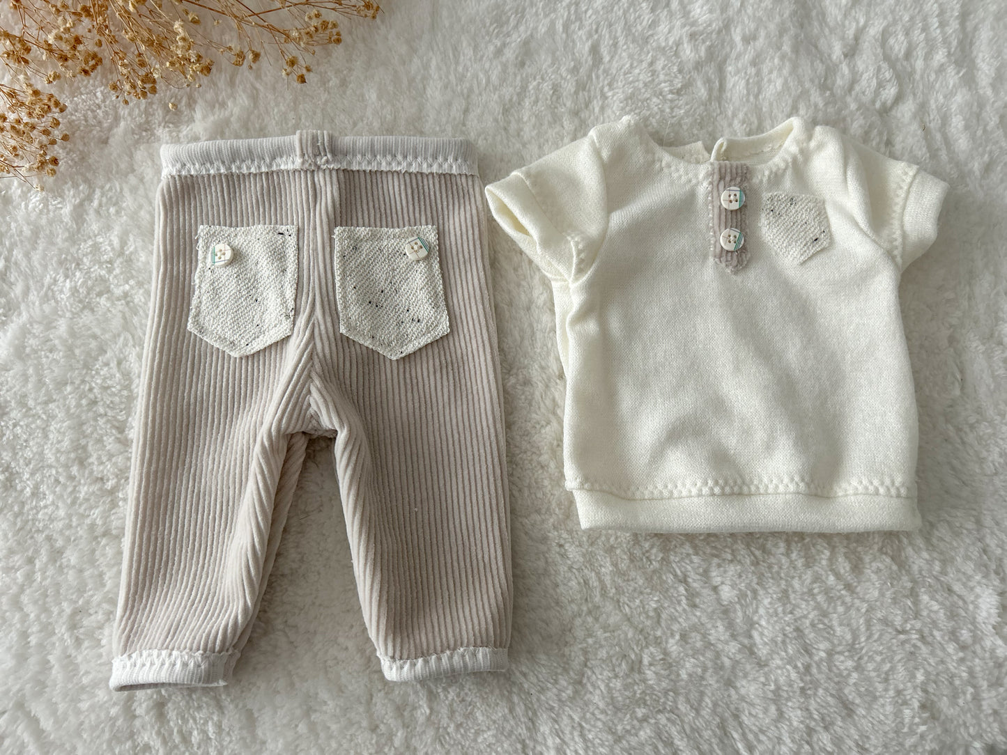 Neutral-toned newborn boy outfit displayed on wooden tray with dried flowers