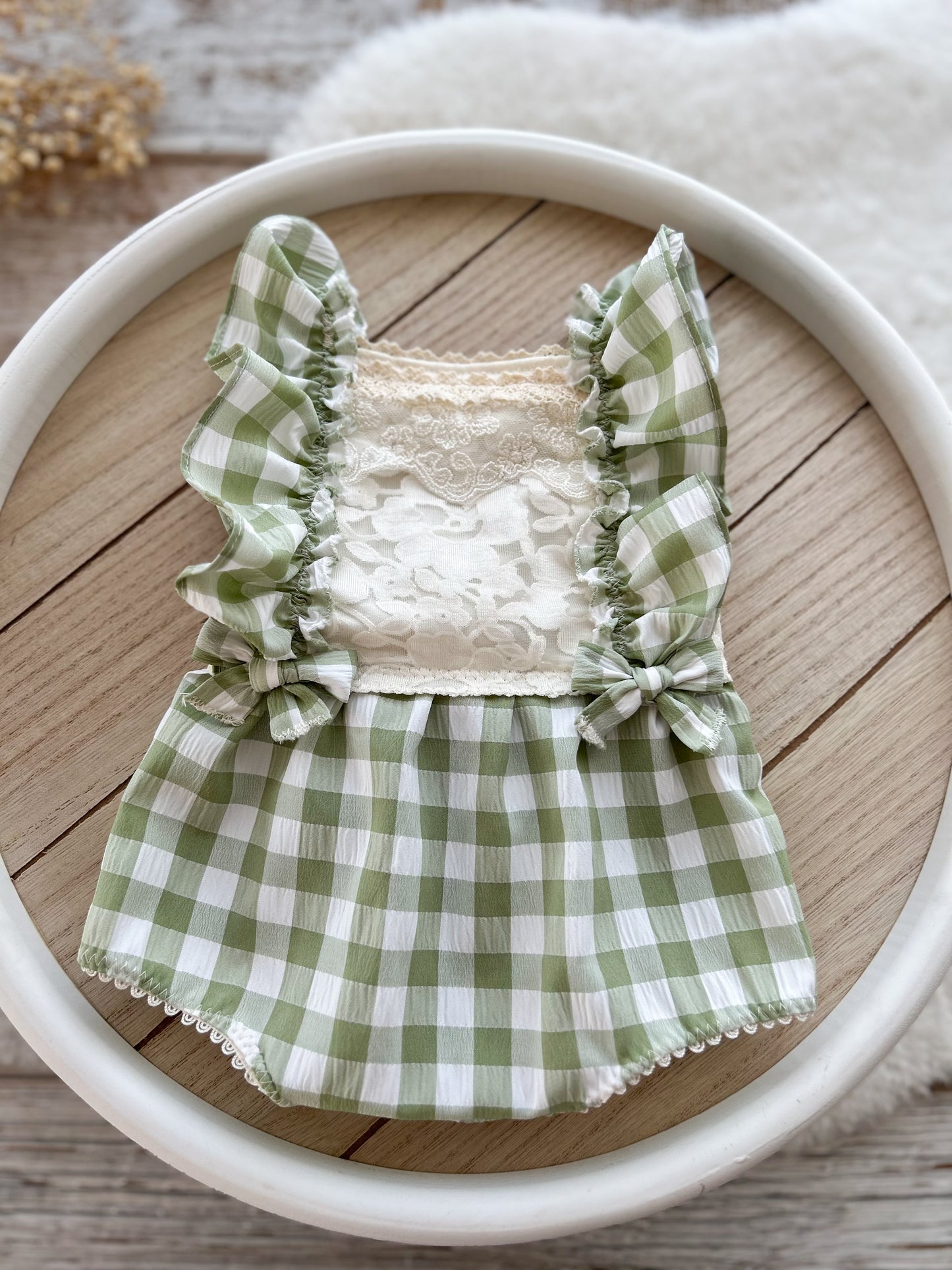 Green gingham ruffled baby romper and matching pillow set for newborn photography, styled in a round bowl on a wood backdrop