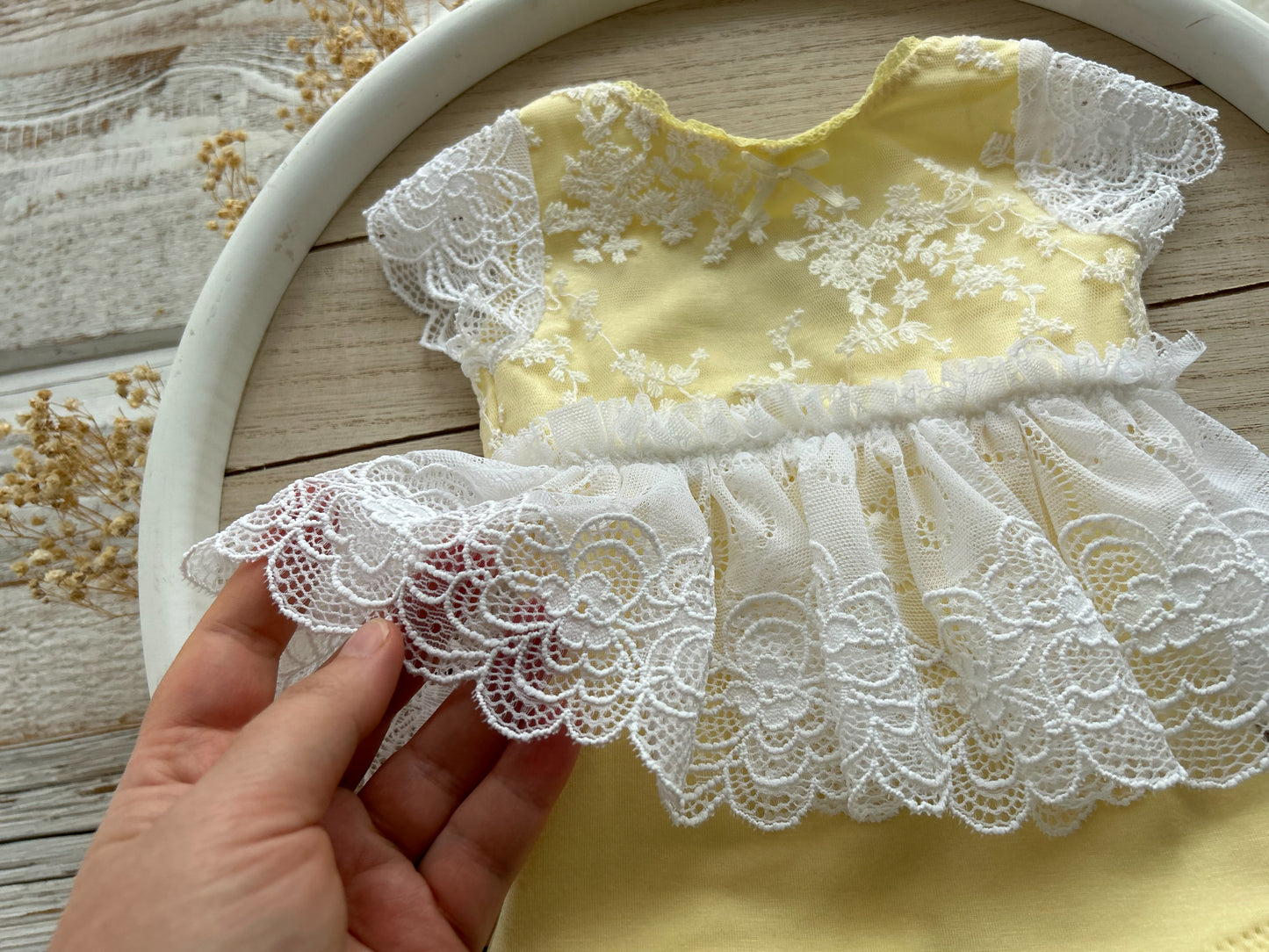 Newborn yellow lace romper with white embroidered lace skirt, displayed on wooden background