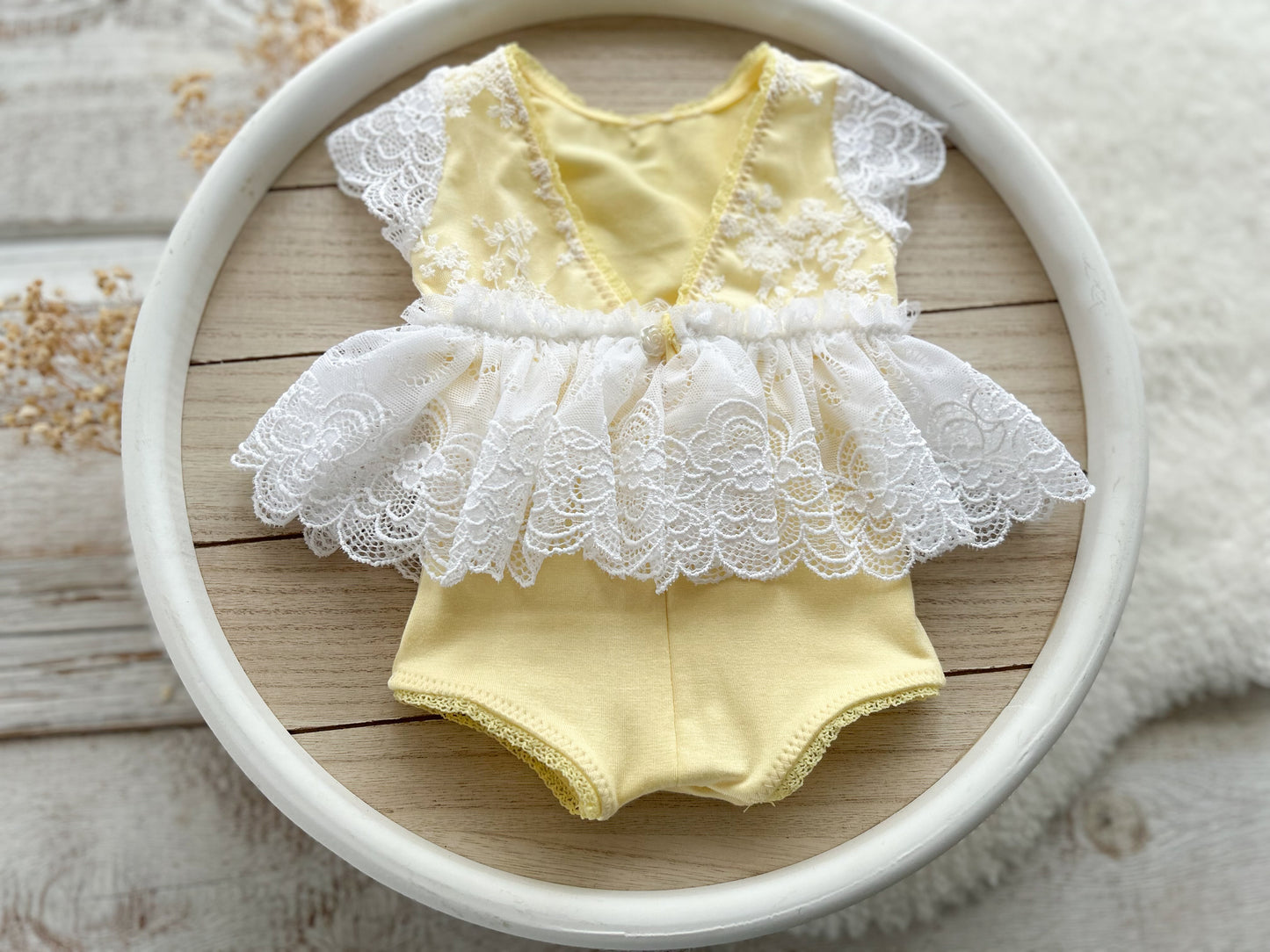 The back of newborn romper in pale yellow color with white floral lace for the skirt and top part.