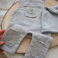 Gray textured romper with button details and knee patches held over a wooden surface
