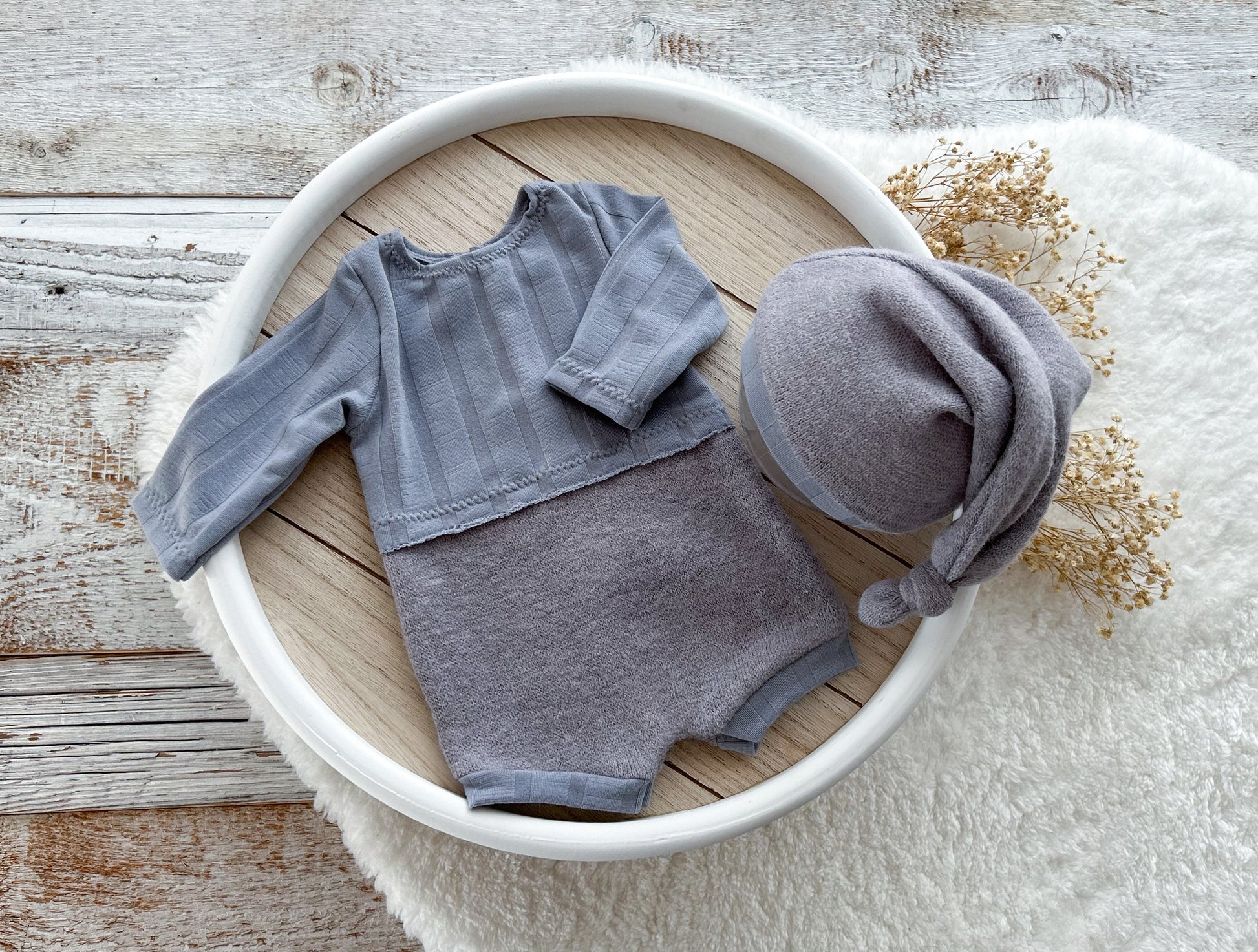 Gray baby outfit with hat in a white bowl on a wooden surface