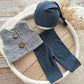 Newborn photography outfit set with blue textured pants, matching hat, and gray curly vest with wooden buttons, styled on a white tray.