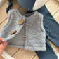 Small gray knitted vest with buttons held by a hand on a wooden surface.