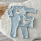Back view of the newborn romper showing buttoned opening, displayed on a wooden tray.