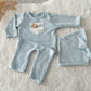 Light blue knit newborn romper with rustic lace patch and wooden button, paired with sleepy hat.