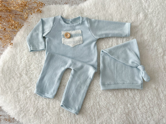 Light blue knit newborn romper with rustic lace patch and wooden button, paired with sleepy hat.