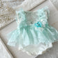 Mint green baby dress with lace details on a textured surface