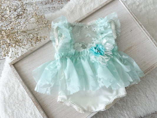 Mint green baby dress with lace details on a textured surface